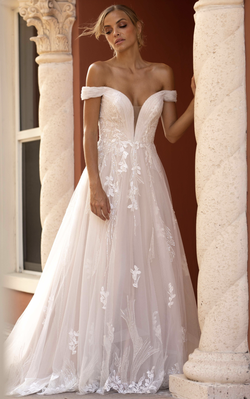 Light, airy, and endlessly romantic — this off-the-shoulder tulle A-line gown features delicate floral appliqués, a plun