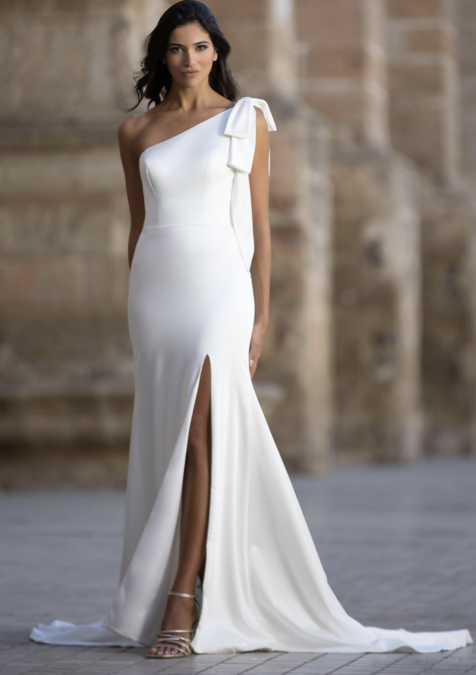 Chic, sophisticated, and striking — this one-shoulder wedding gown features a sleek crepe silhouette, statement bow deta