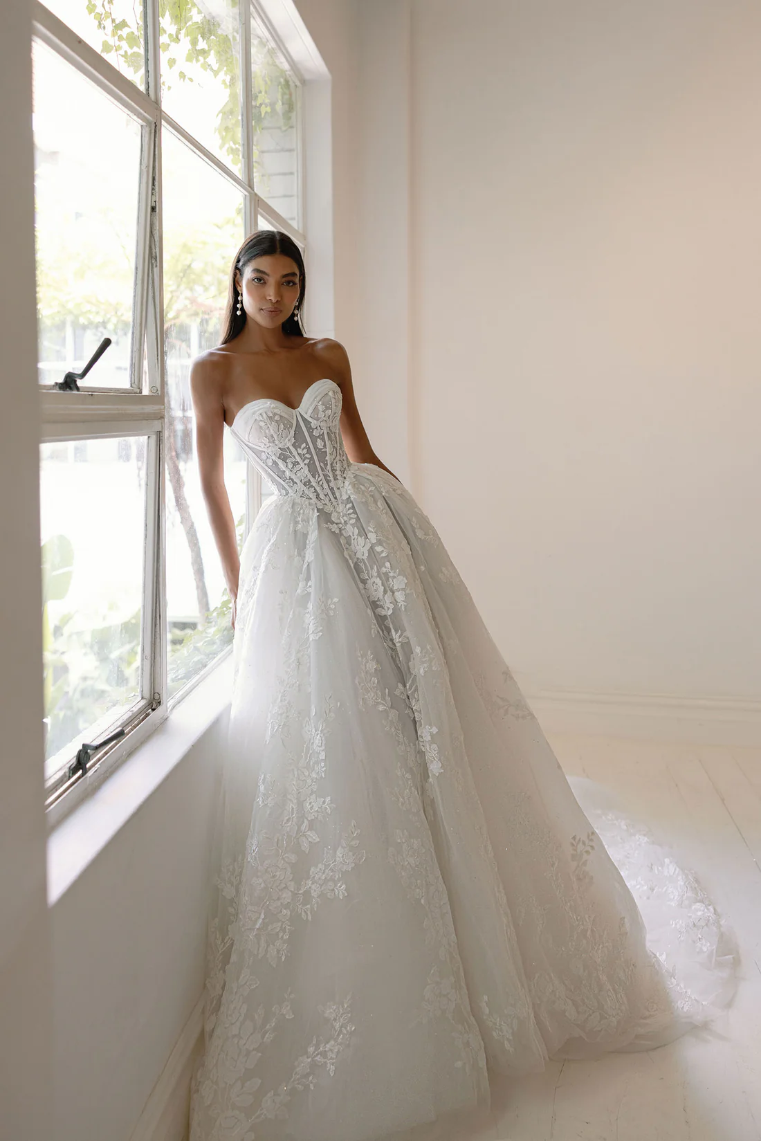 A gown fit for a modern-day princess. Featuring a sheer corset bodice, layered tulle skirt, and delicate floral appliqué