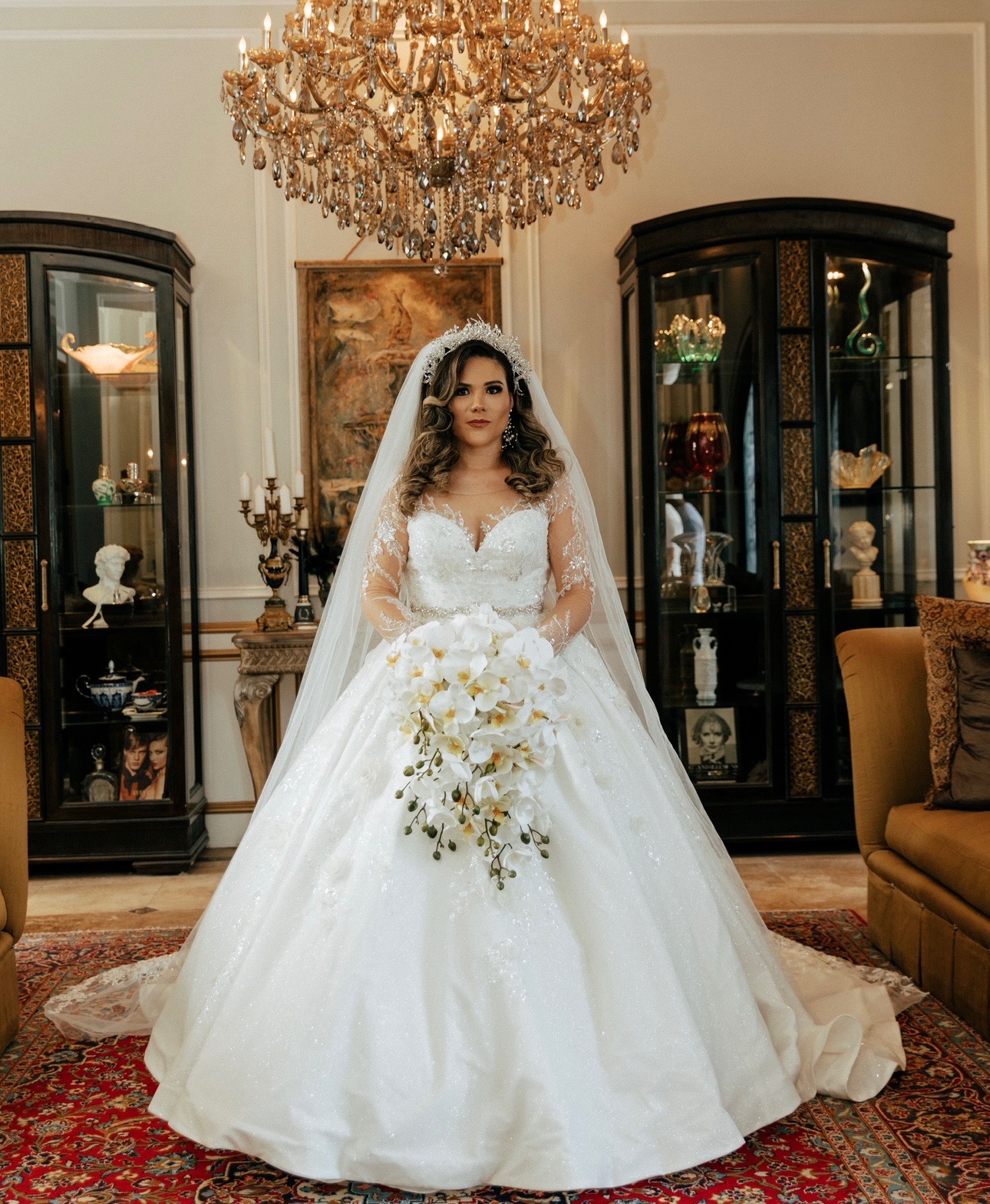 This breathtaking ball gown exudes royalty with its sparkling full skirt, illusion lace sleeves, and sweetheart neckline