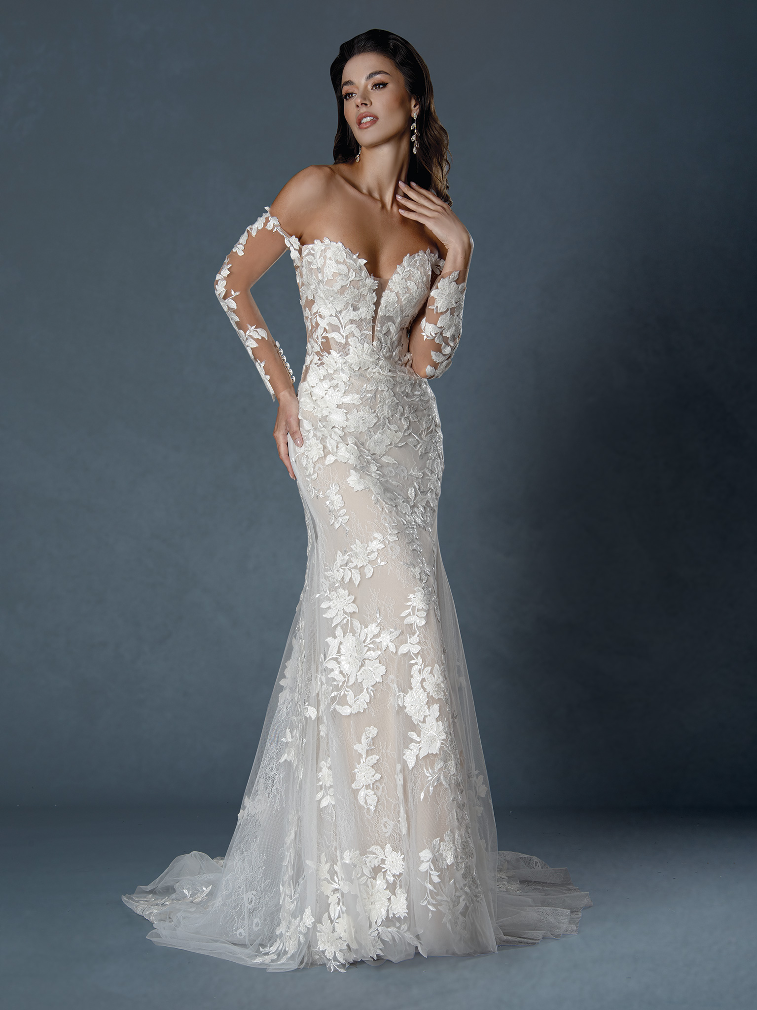 Bold and breathtaking, this off-the-shoulder lace gown features a sheer illusion bodice, romantic long sleeves, and a cu