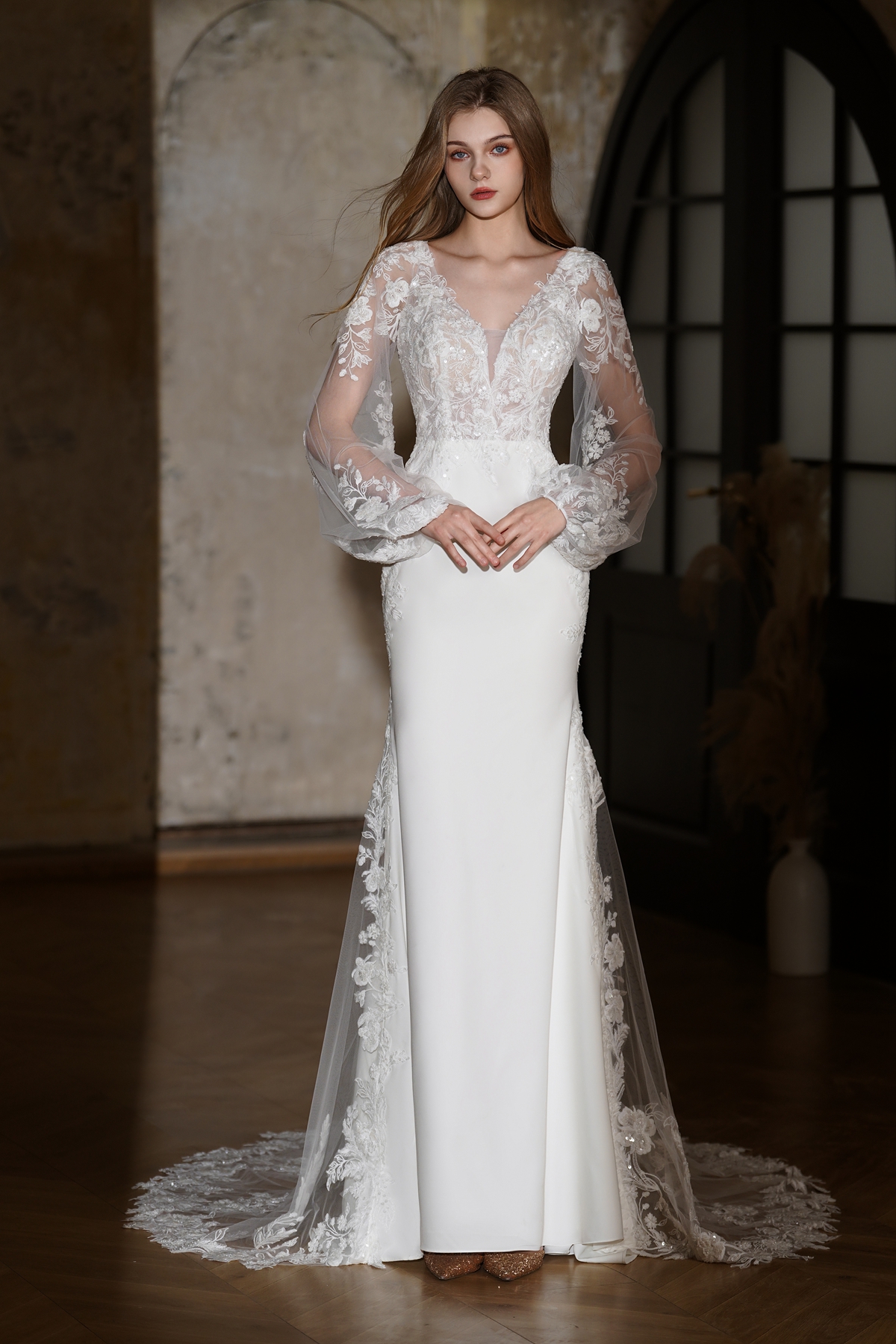 A vision of elegance, this lace long-sleeve wedding gown features a deep illusion neckline, sheer puffed sleeves, and a 