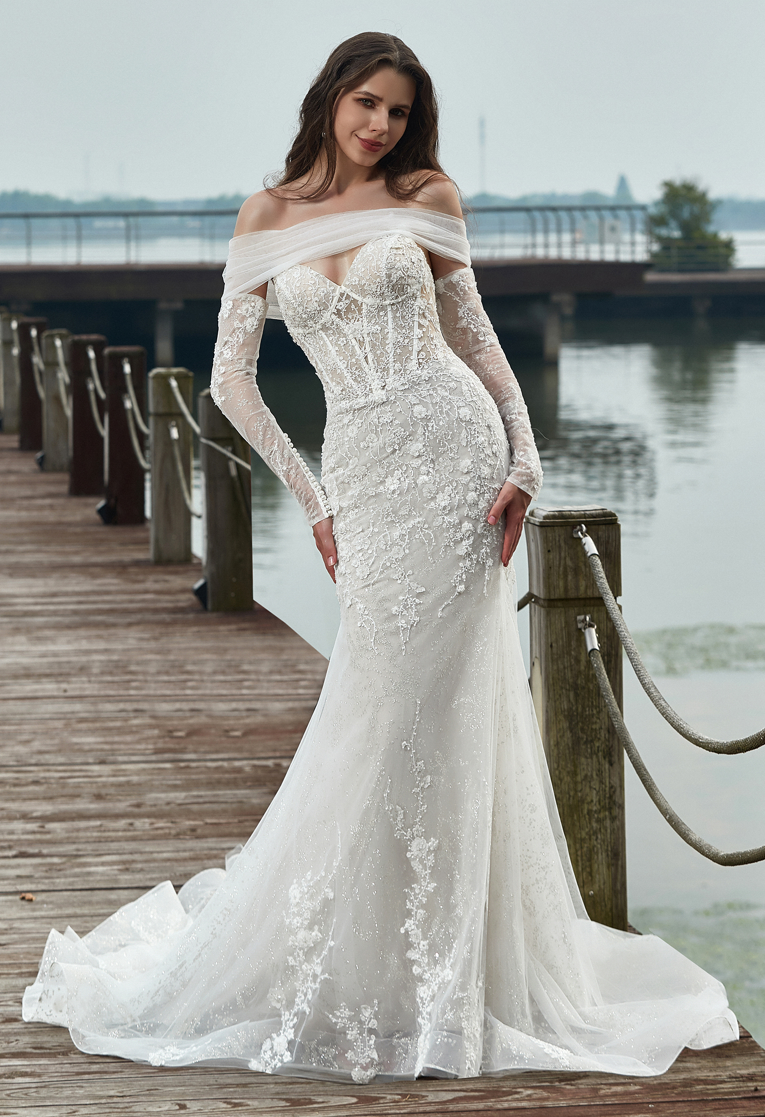 This off-shoulder lace gown shimmers with delicate beadwork and sheer long sleeves. The romantic neckline and fitted sil