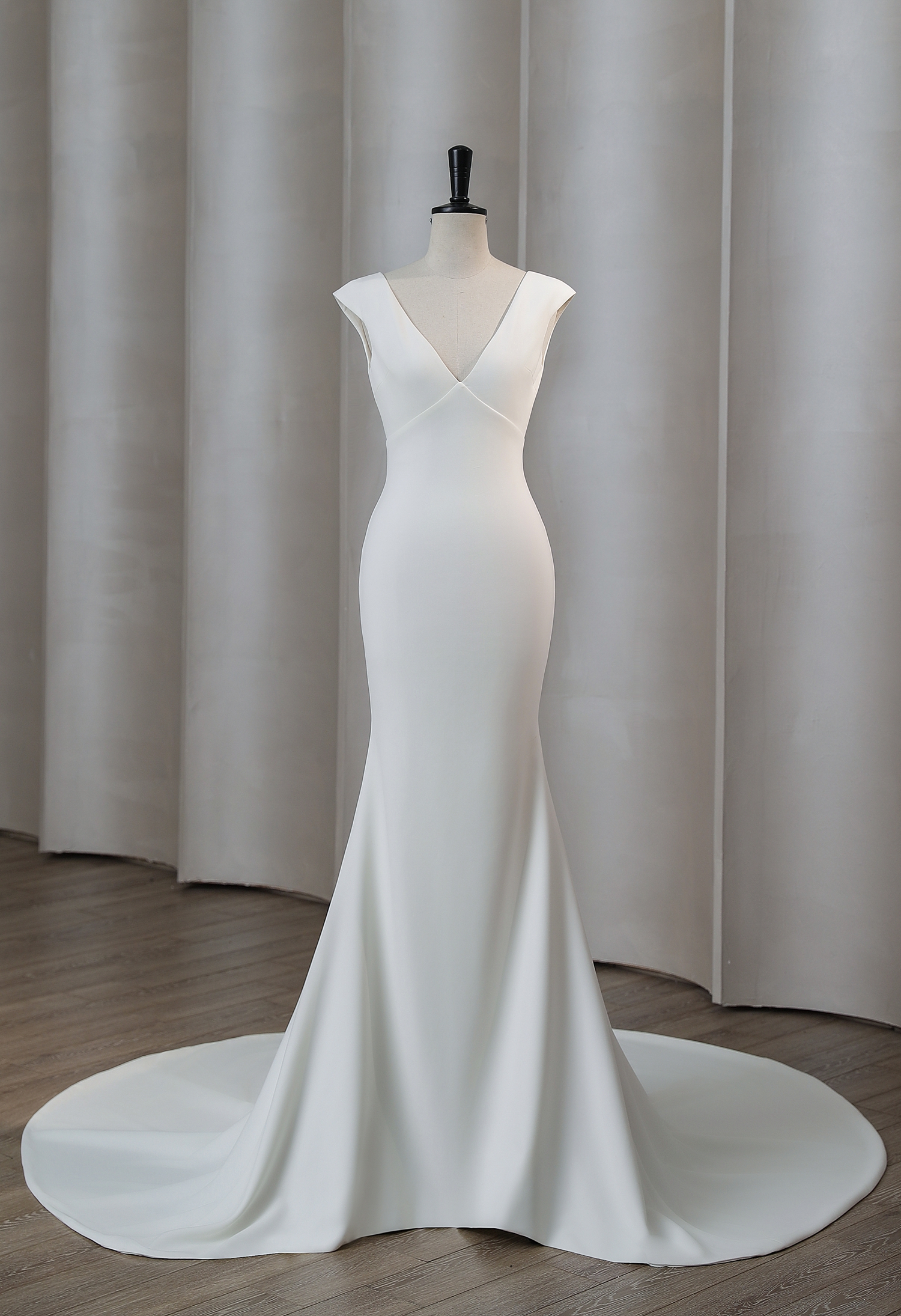 A stunning minimalist crepe wedding gown featuring a deep V-neckline and soft cap sleeves. This elegant silhouette flatt