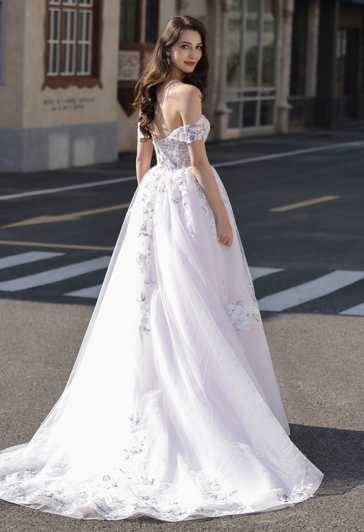 This off-the-shoulder floral A-line wedding dress features delicate lilac lace appliqués layered over a soft ivory base 