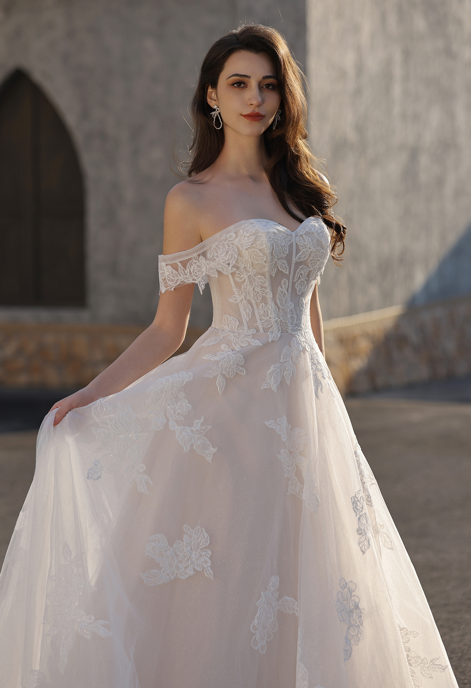 This off-the-shoulder lace A-line wedding dress features a structured bodice with delicate floral lace appliqués and a s