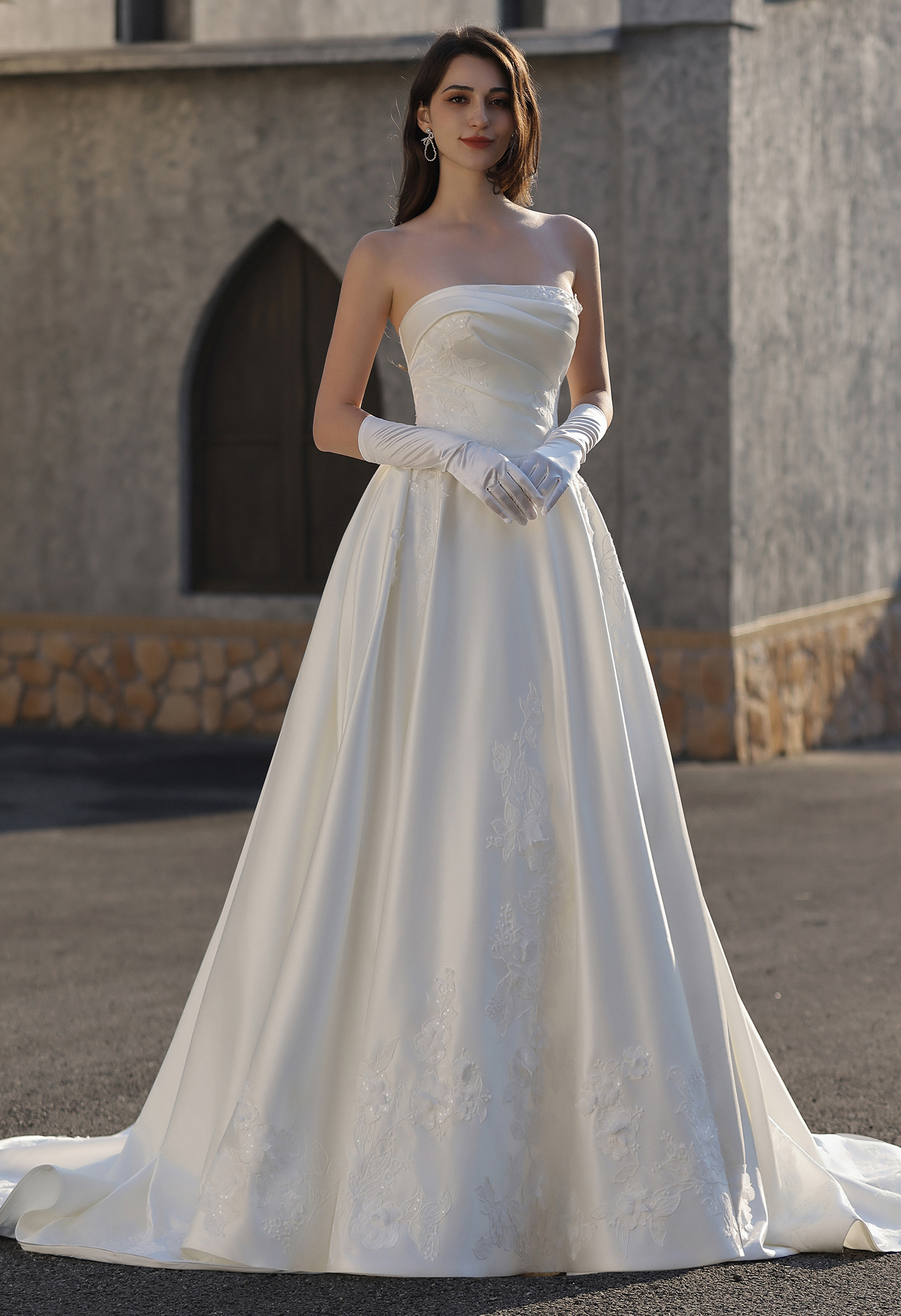 This strapless satin ball gown wedding dress features a clean, structured bodice and a full flowing skirt accented with 